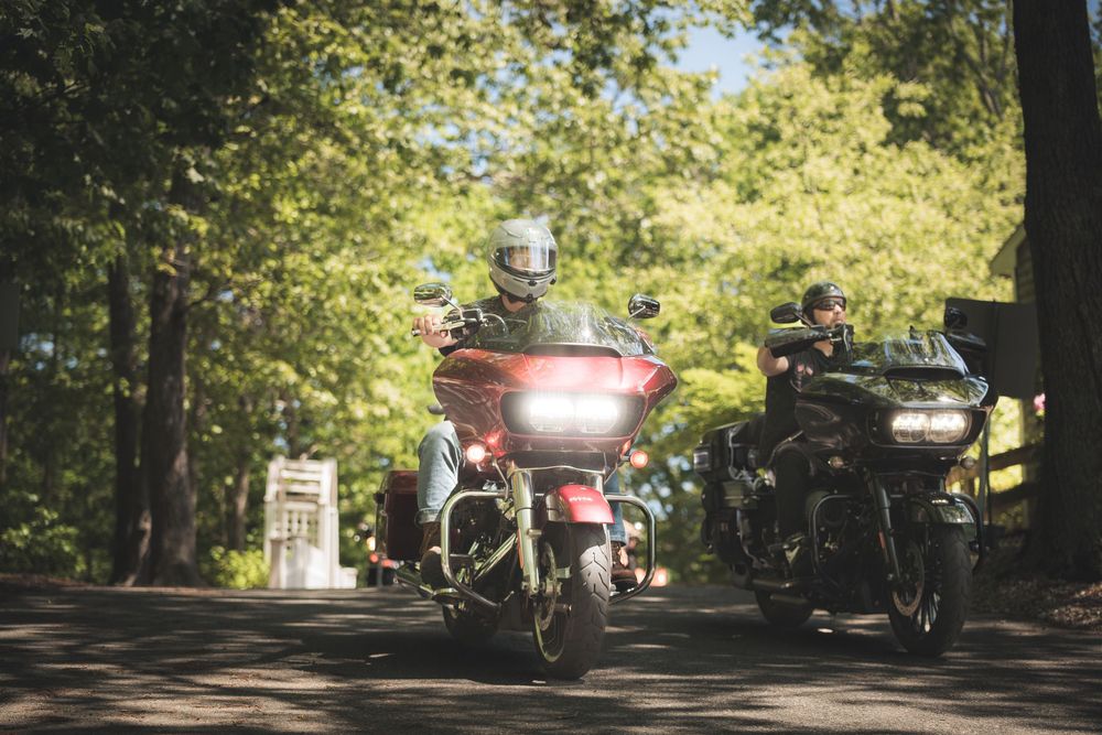 Motorcycles riding through a tree-lined road with sunlight filtering through.
