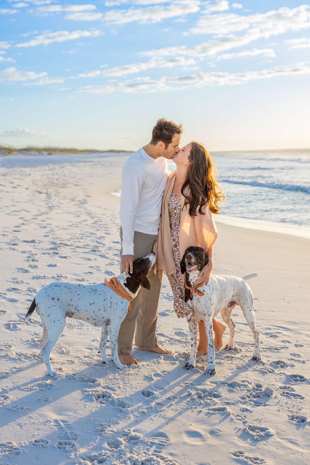 Romantic couple shares tender moments together while walking their dog on a white sandy beach at sunset.