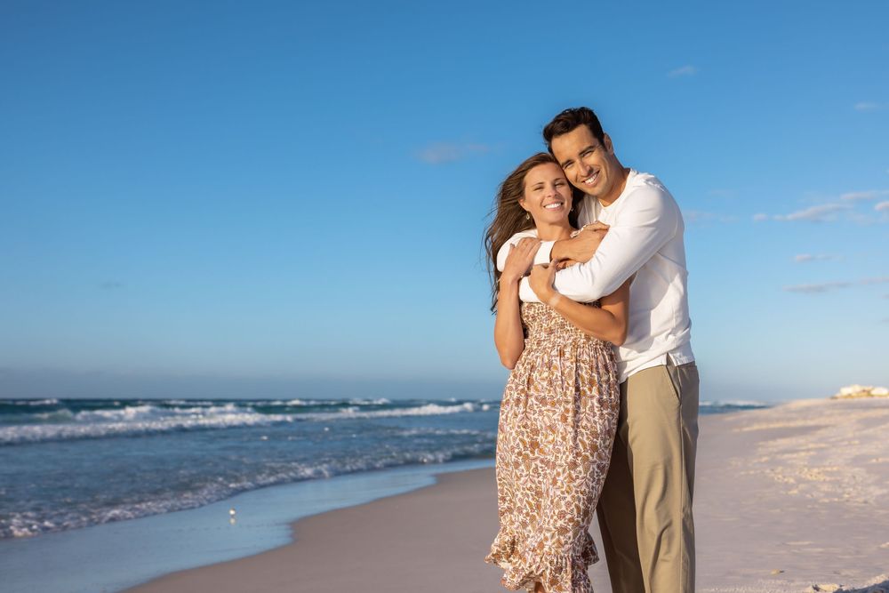 A couple in beachwear poses for romantic photos together along a sandy shoreline at sunset.