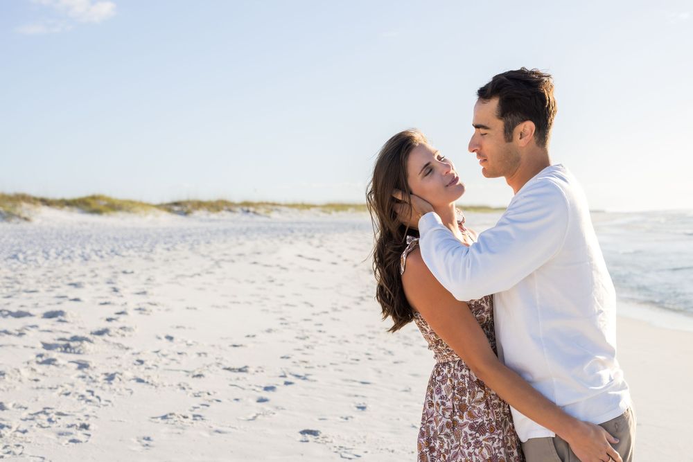 Couple in love sharing intimate moment on white sandy beach at sunset.