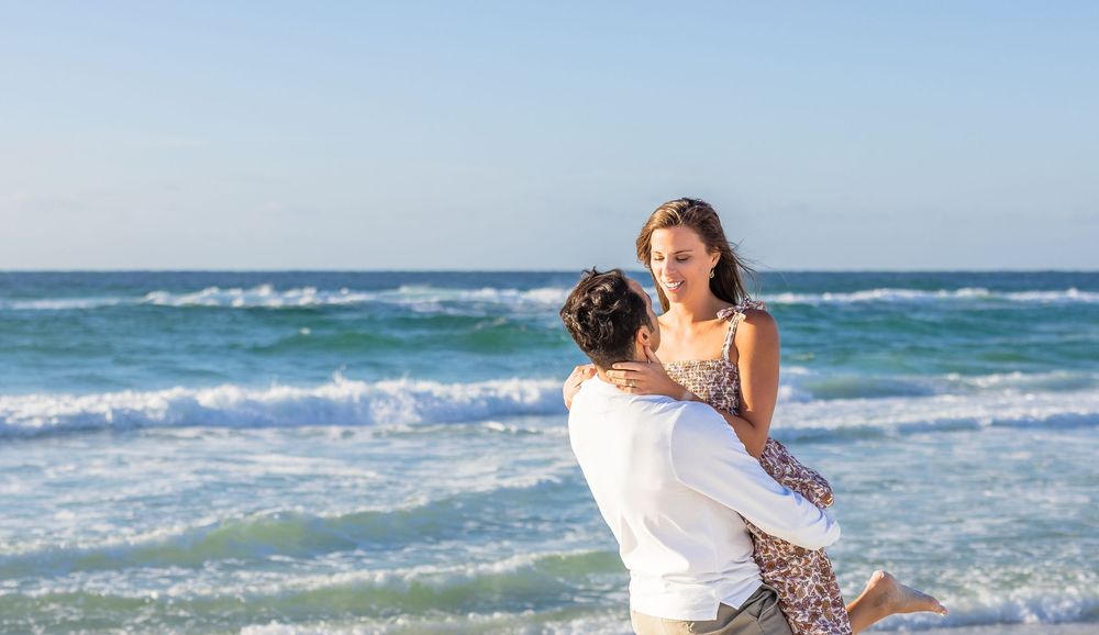 A person in a white dress runs joyfully along the beach with waves crashing in the background.