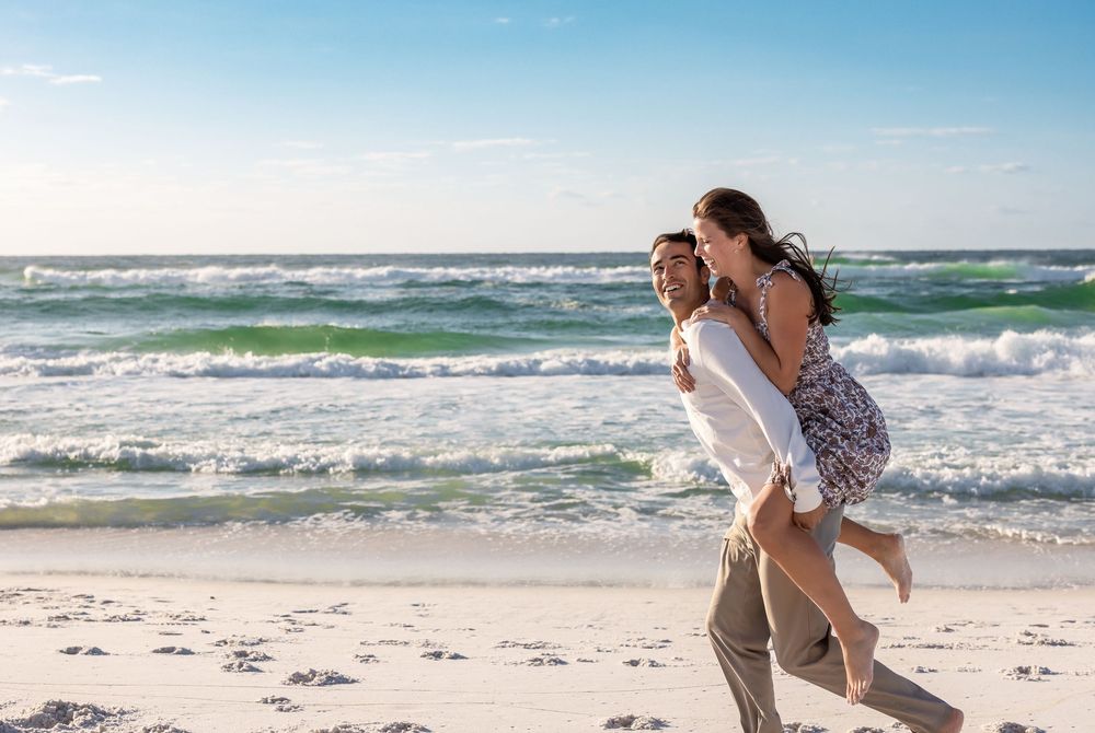 Couple embracing on a sunny beach with white sand and crashing waves in the background.