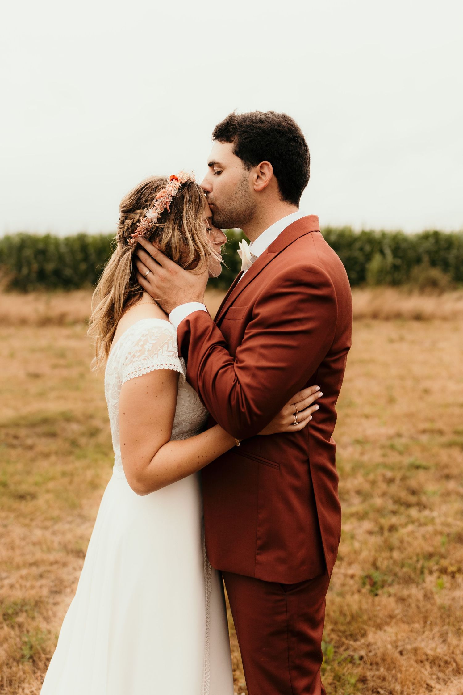 Intimate wedding portrait in a rustic field with bride in white dress and groom in rust-colored suit.