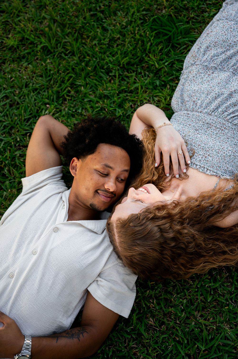 A couple laying on green grass sharing tender moments together.