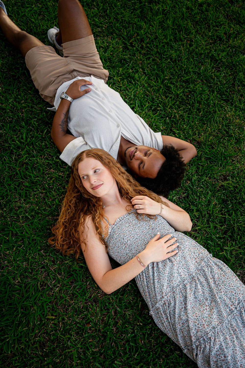 A couple in casual attire laying on grass during an outdoor photoshoot.
