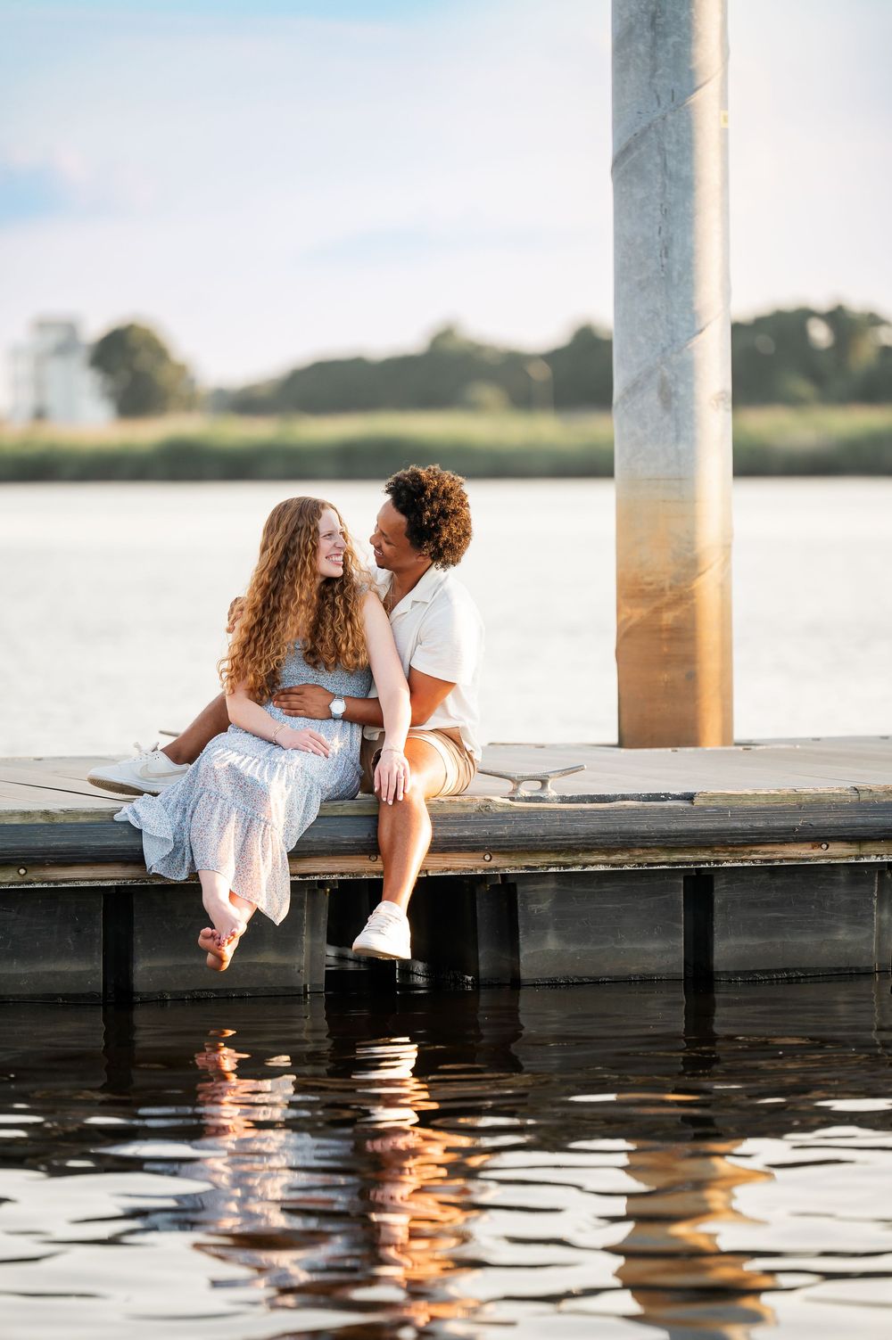 A couple shares romantic moments on a wooden dock by the water at sunset.