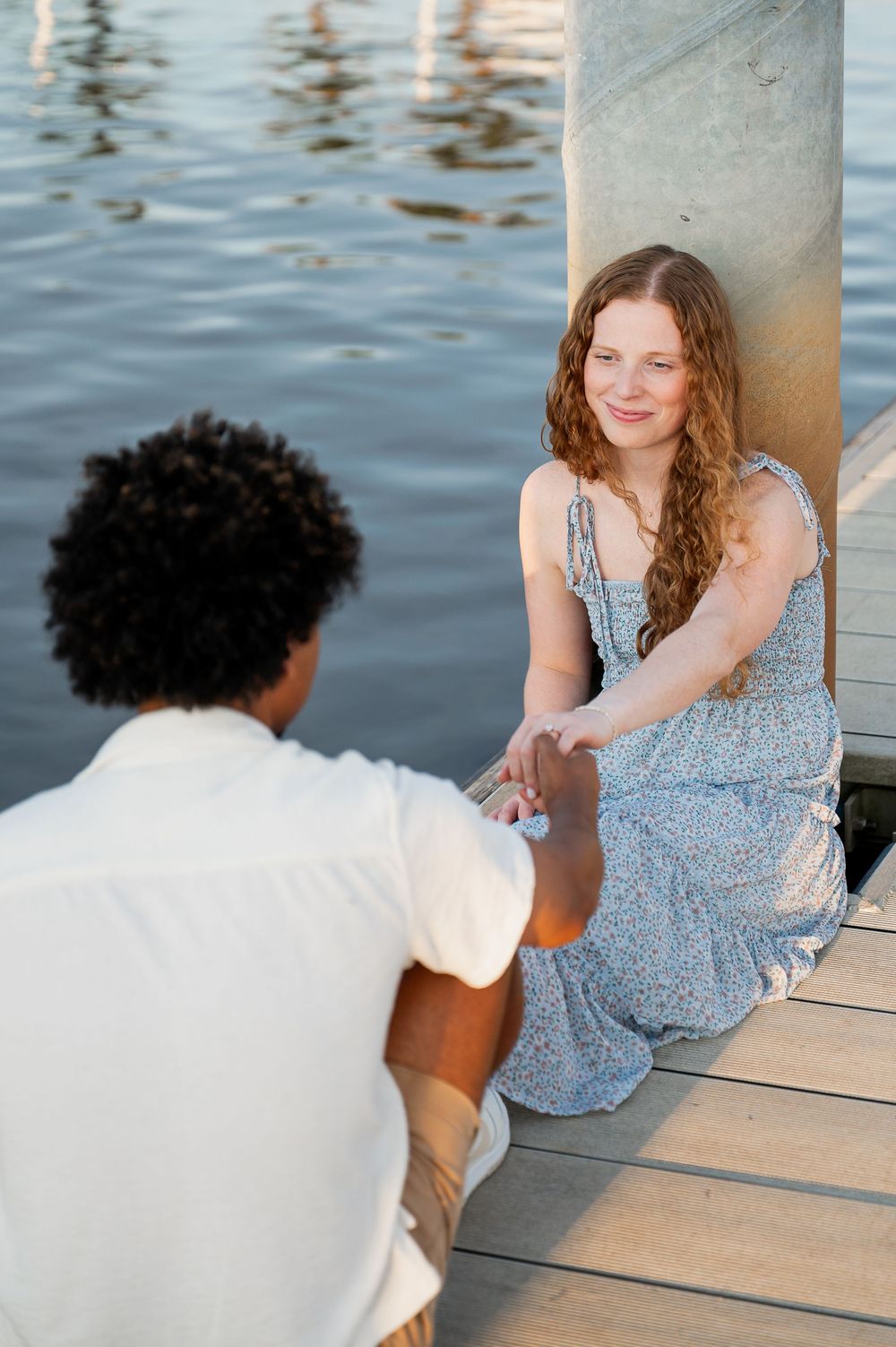 A couple sits together on a wooden dock overlooking calm waters.