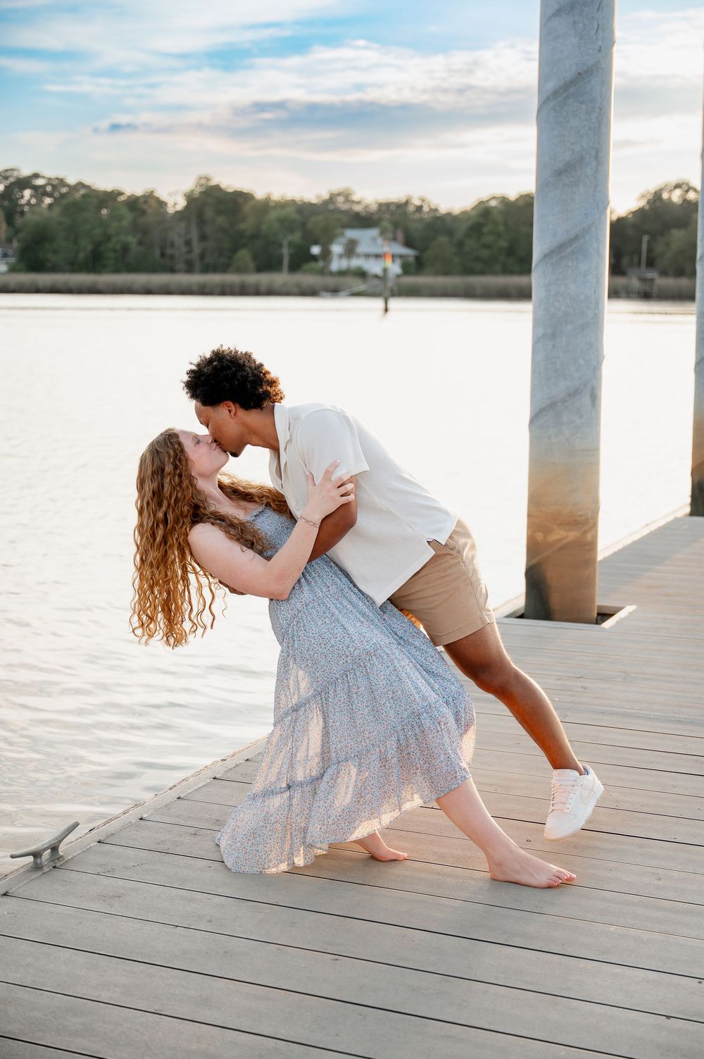 A playful couple dances together on a waterfront dock during golden hour.