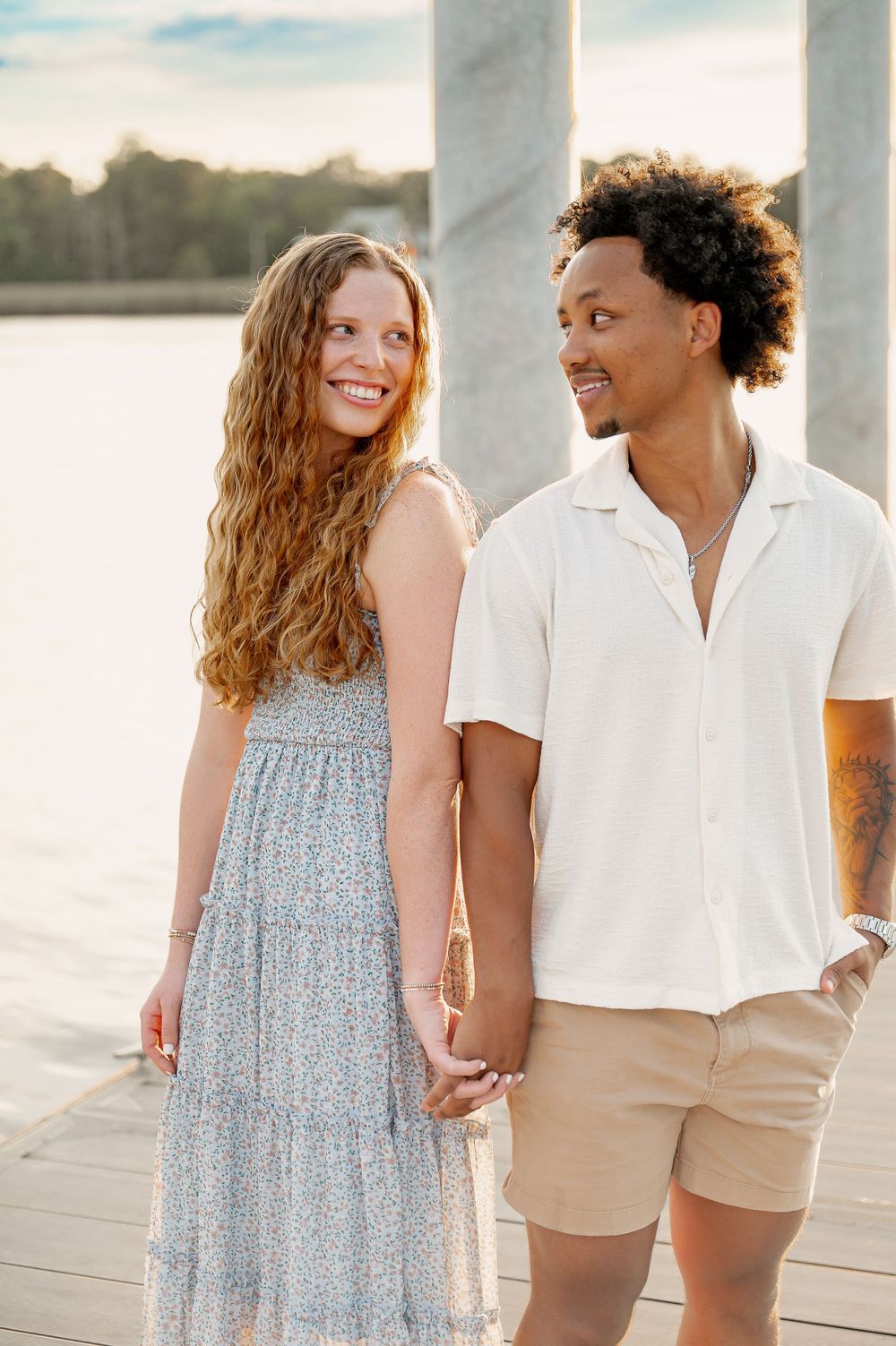 A couple in summer attire shares joyful moments on a dock during sunset.