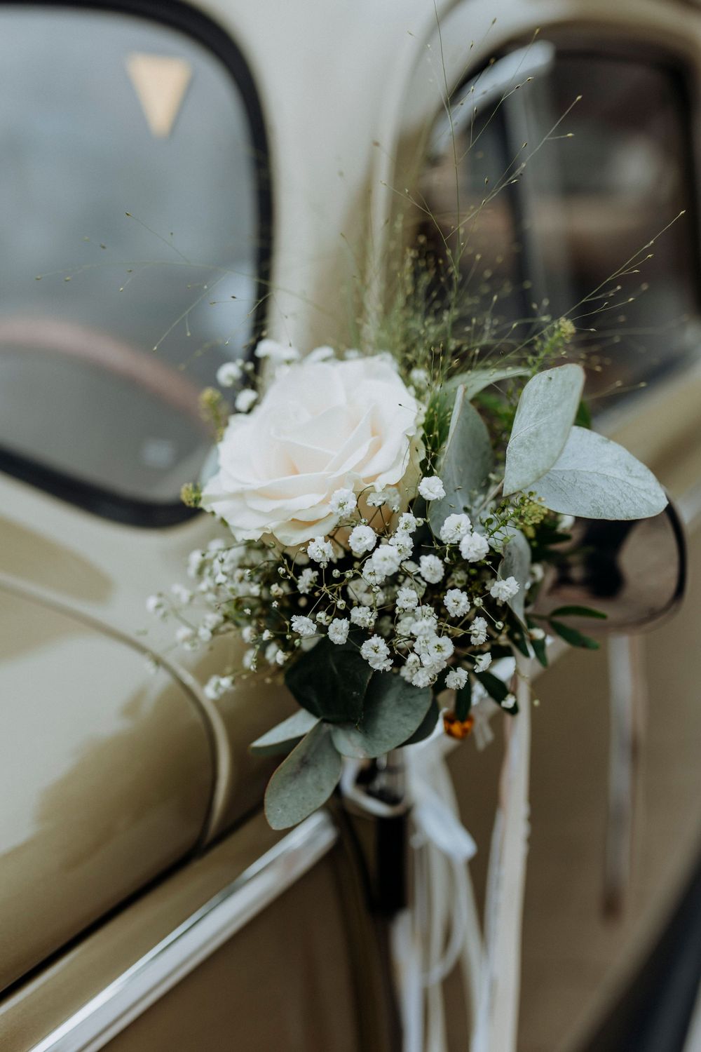 Delicate floral decorations with roses and baby's breath adorning a car's side mirror.