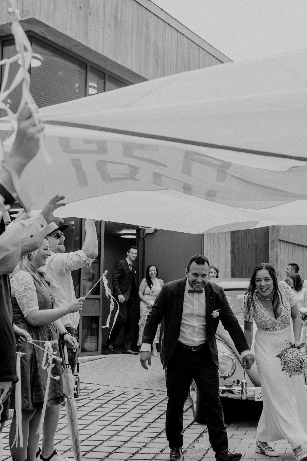 Wedding guests holding up a large white banner during an outdoor celebration.