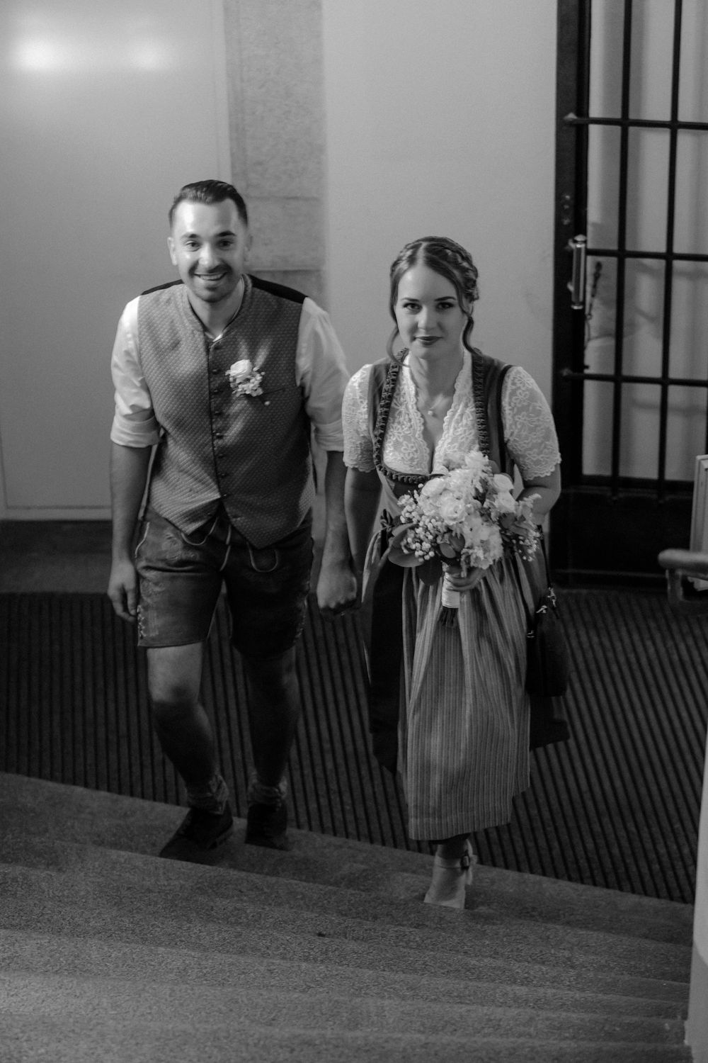 Black and white photo of couple walking down hallway in traditional German attire.