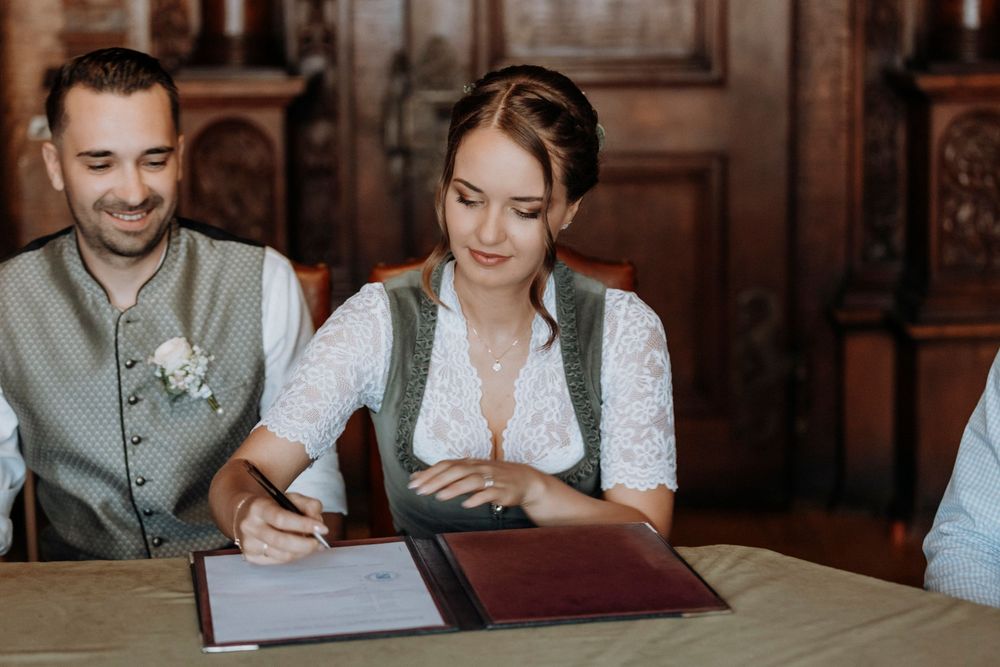 Wedding couple signing documents at a traditional wooden table.