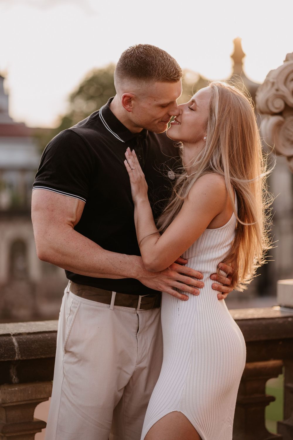 Romantic couple embraces and kisses during golden hour sunset on a rustic wooden deck.