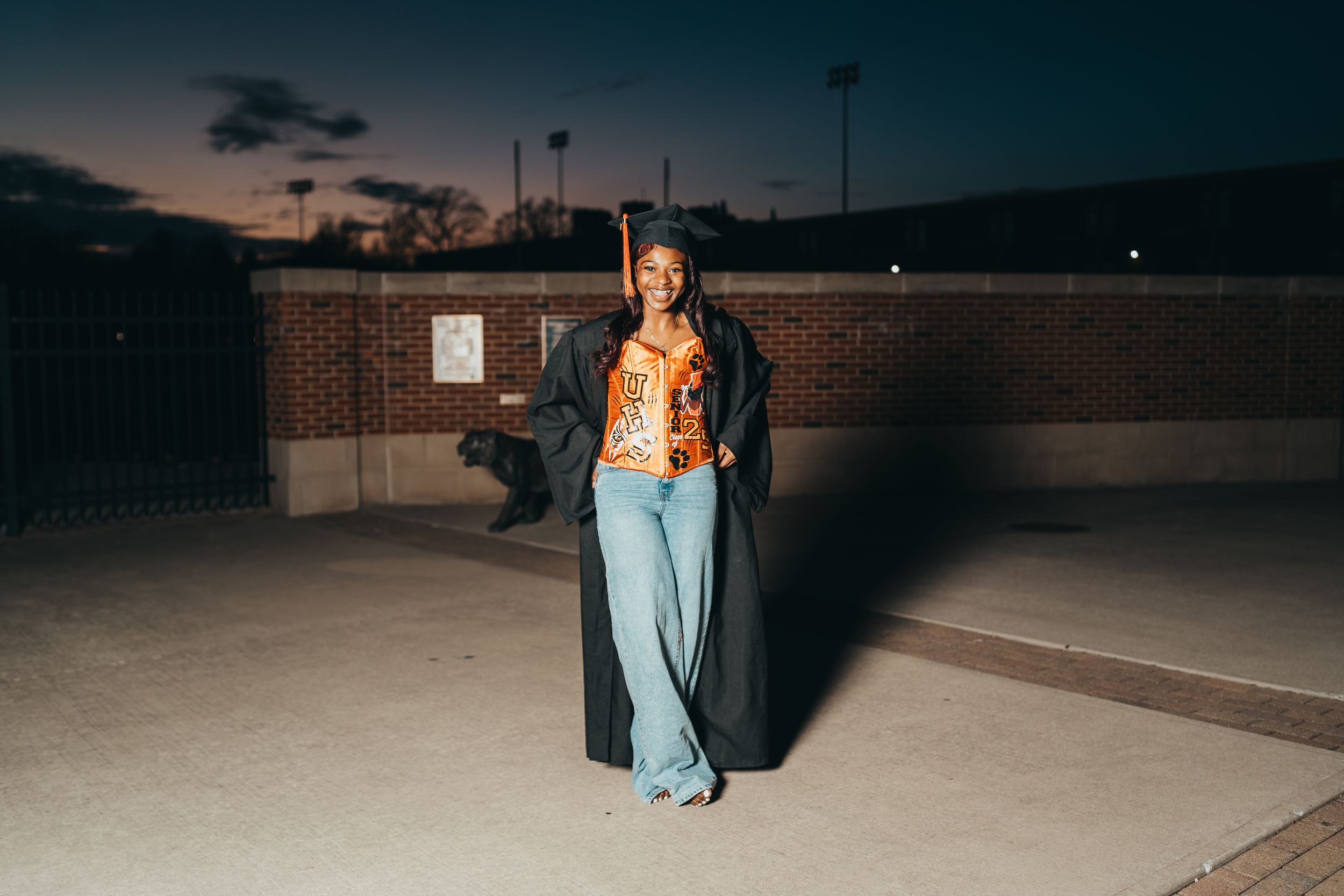 A person in bell bottom jeans and jacket poses at night in front of a brick building.
