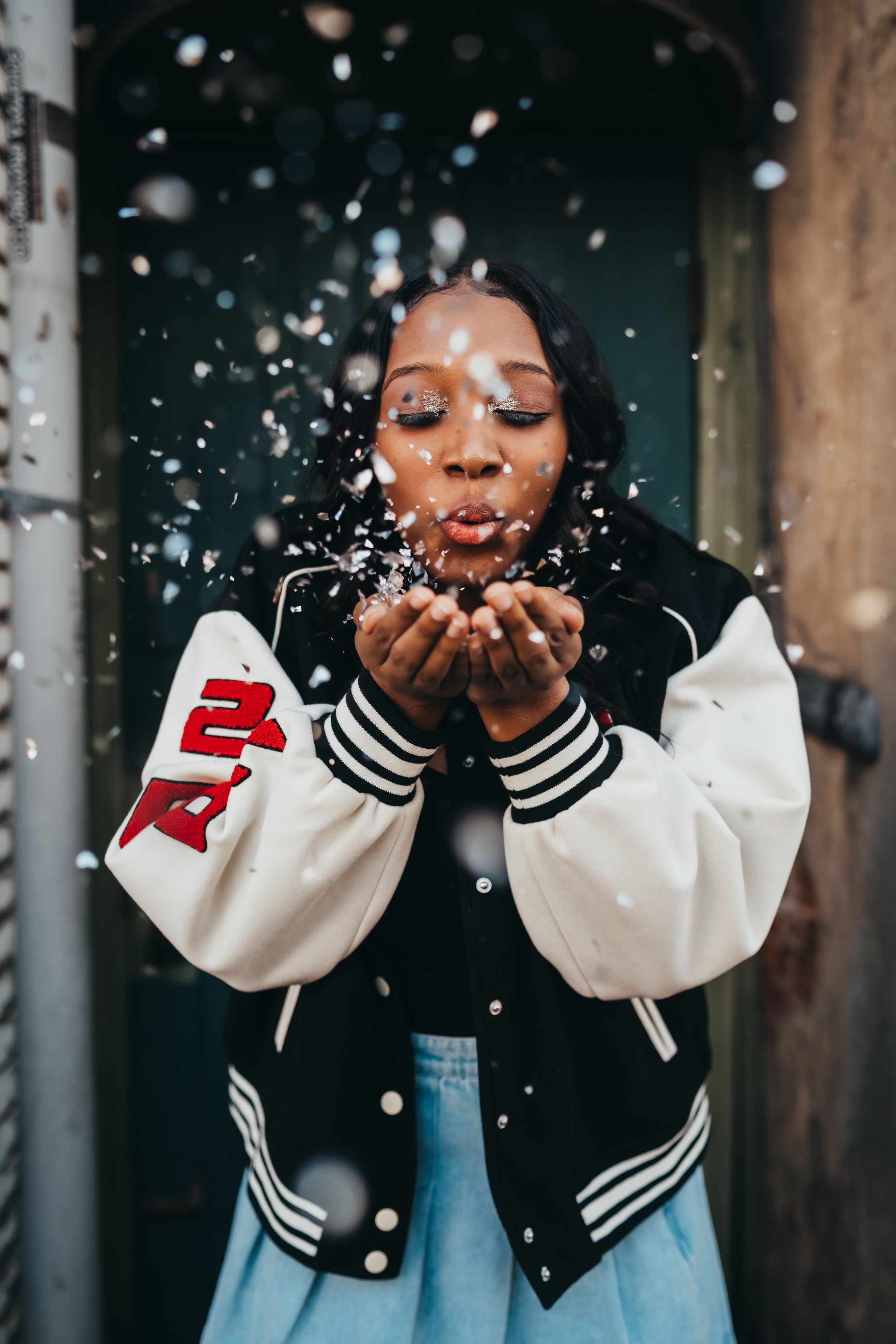 Person in varsity jacket blowing glitter in winter photoshoot. graduate session