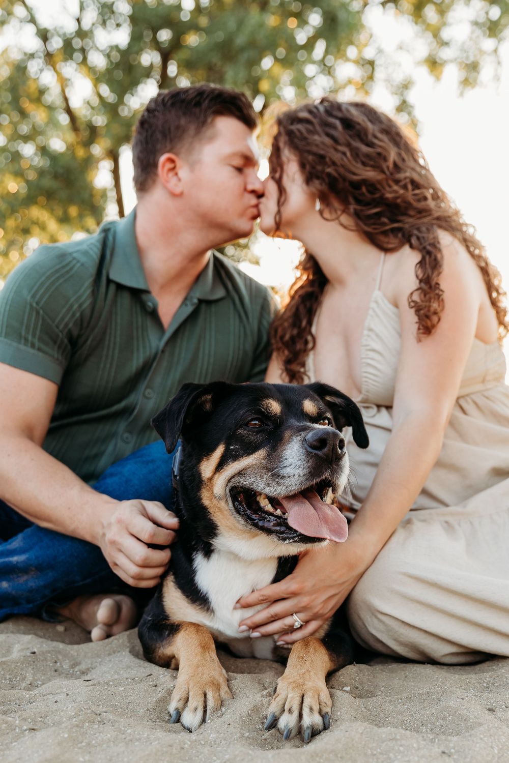 A happy black and white dog lies in the sand as a couple shares an intimate moment at sunset. Cleveland Maternity Photographer