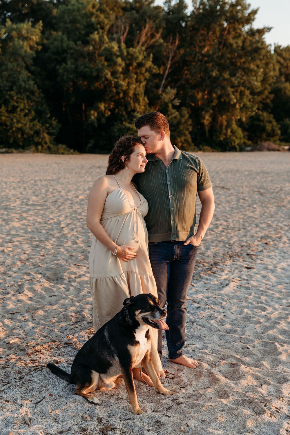 Couple sits on beach sand with their dog during a golden sunset photoshoot.