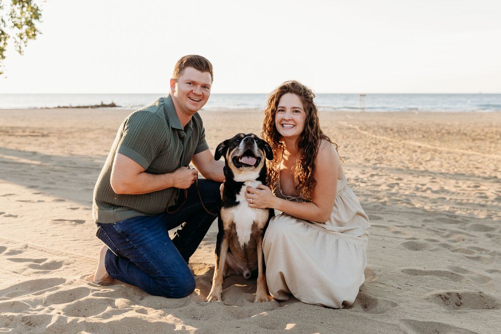 A couple and their dog share joyful moments together on a sandy beach at sunset. Cleveland Maternity Photographer