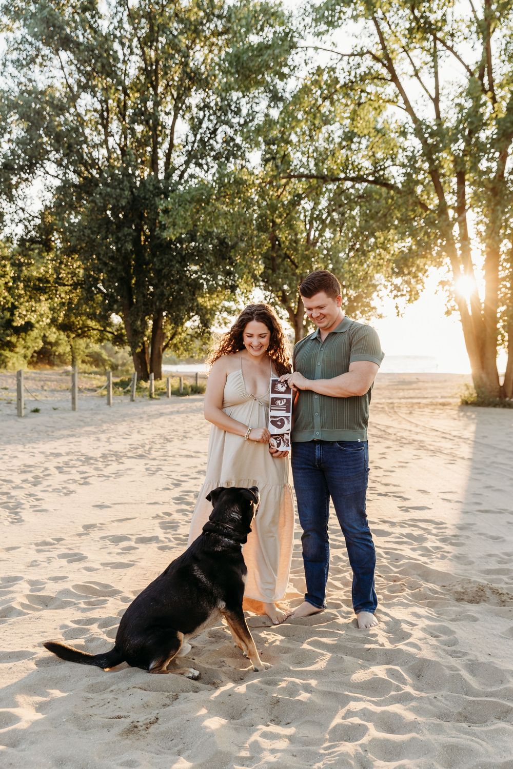 Couple and their black dog enjoying a playful moment together on a sandy beach at sunset. Cleveland Maternity Photographer