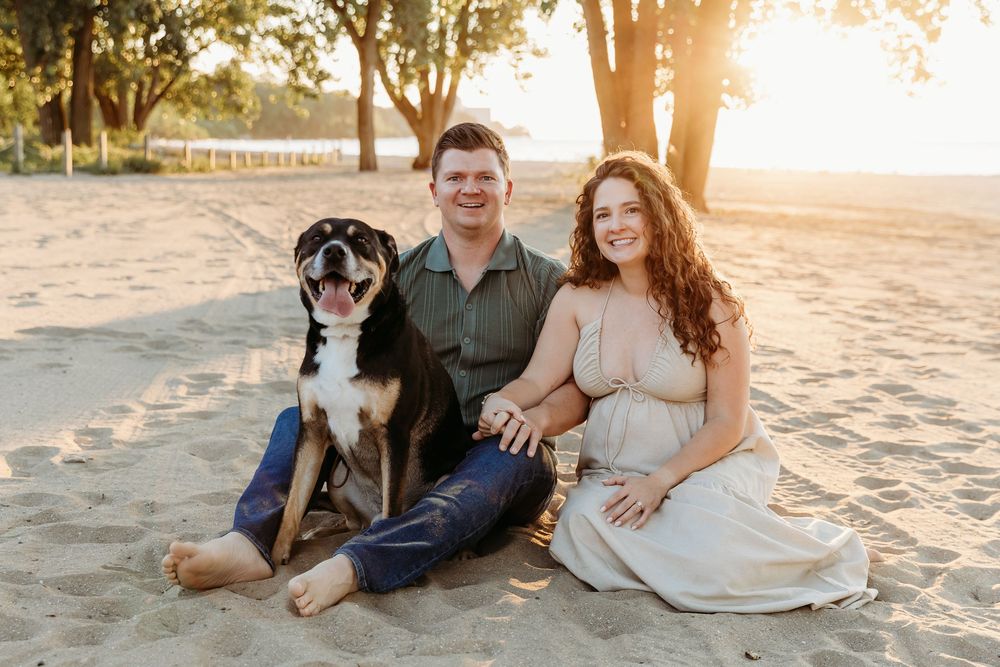 A couple sits on the beach with their dog at sunset creating a romantic silhouette against the golden sky. Cleveland Maternity Photographer