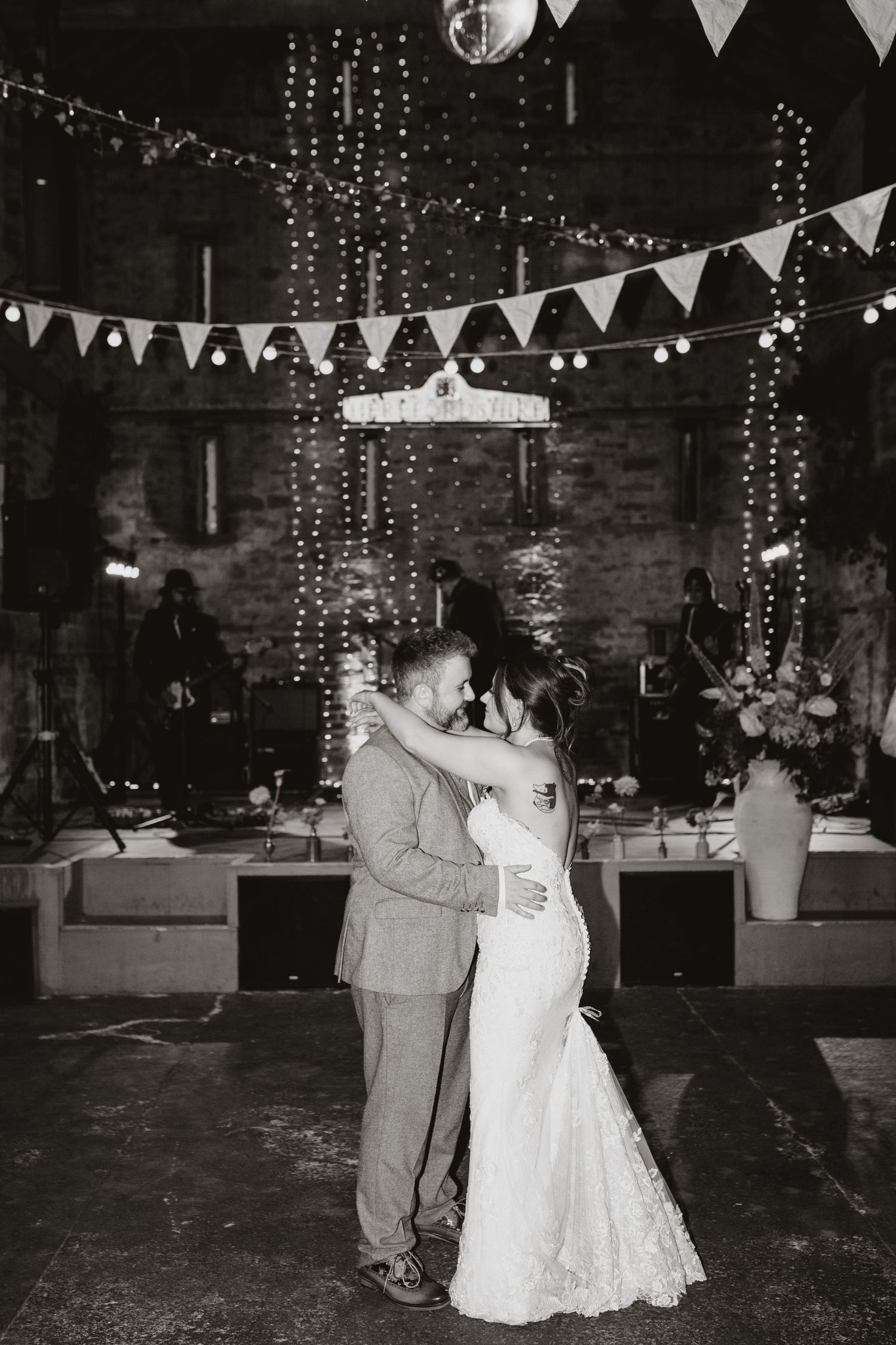 A couple shares their first dance at a rustic wedding reception decorated with string lights and bunting flags.
