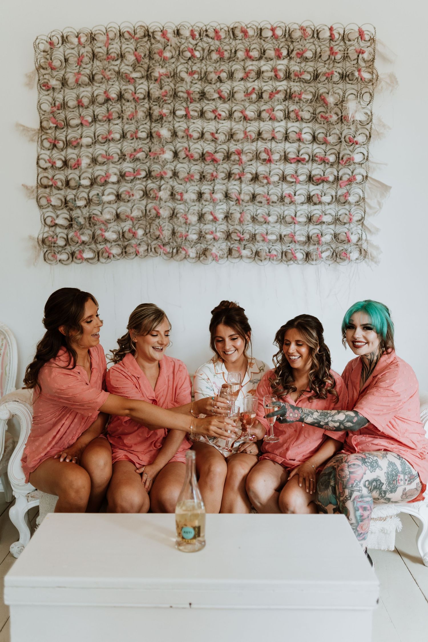 Bride & Bridesmaids in matching pink robes sits together, laughing on morning of wedding at Lyde Court, Hereford.