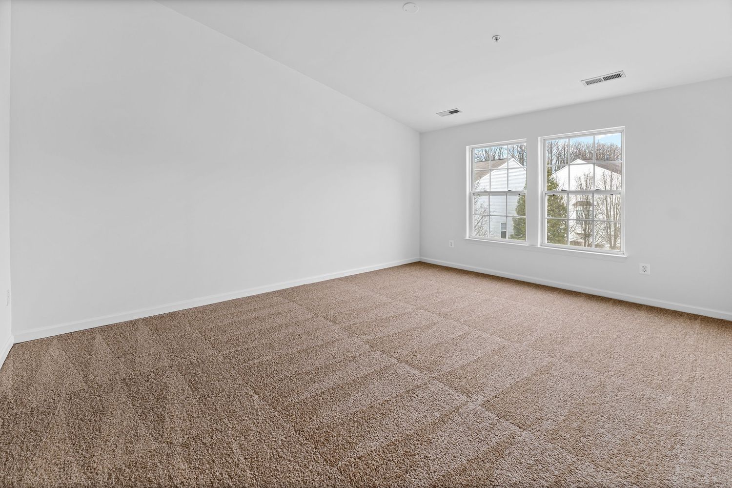 Empty room with beige carpeting, white walls, and large windows showing exterior views.