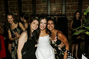 A group of wedding guests in formal attire celebrating at an evening reception with brick walls in the background.