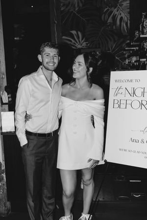 Black and white photo of people at a party with welcome signs and decorative elements visible in the background.