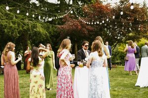 Guests in colorful summer dresses gather at an outdoor garden party under string lights during a daytime celebration.