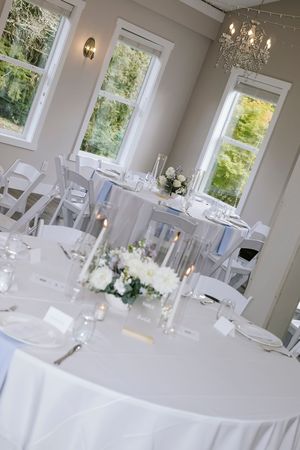 Elegant white wedding reception venue with round tables, crystal chandeliers and large windows letting in natural light.