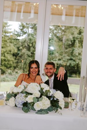 Elegant wedding table setting with white floral centerpiece and eucalyptus greenery in front of bright windows.