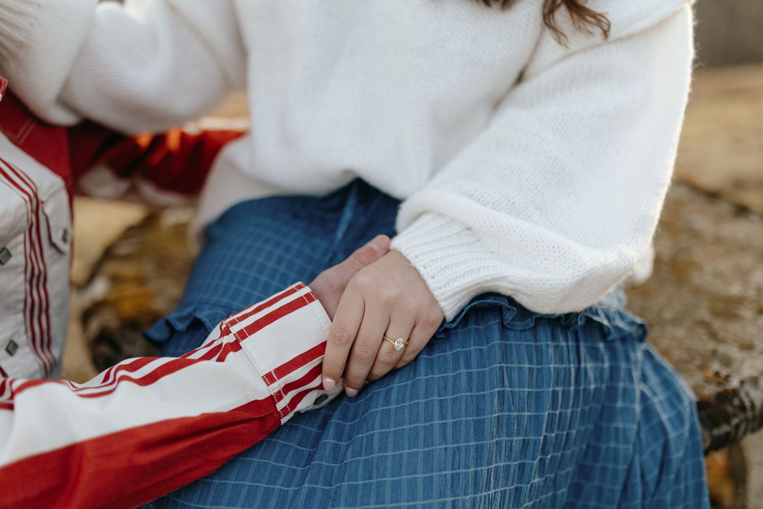 Close-up view of someone wearing a white sweater and blue plaid skirt sitting on a surface.