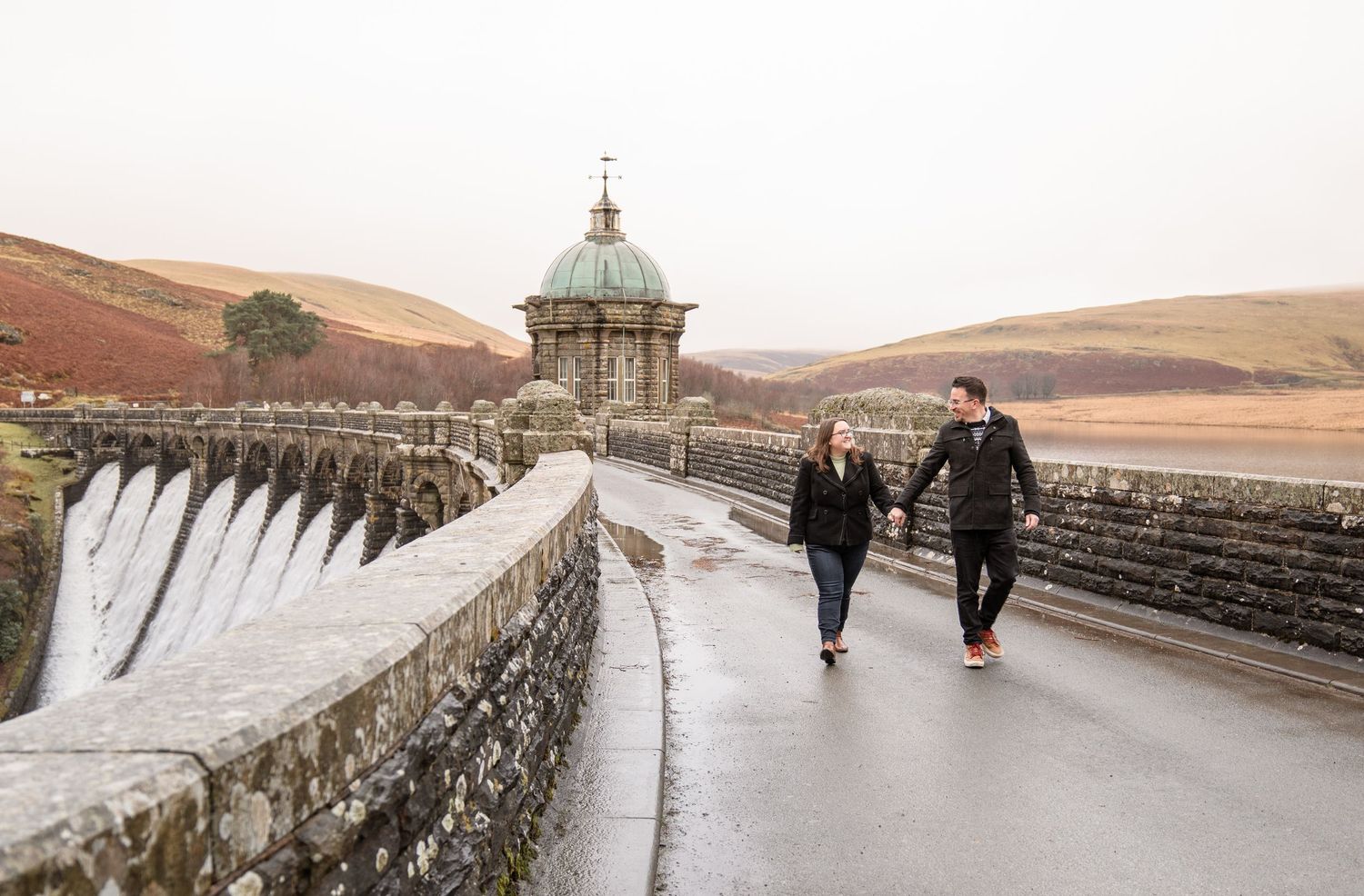 A series of panoramic views showing people walking along the stone walls of a large reservoir dam in a rural setting.