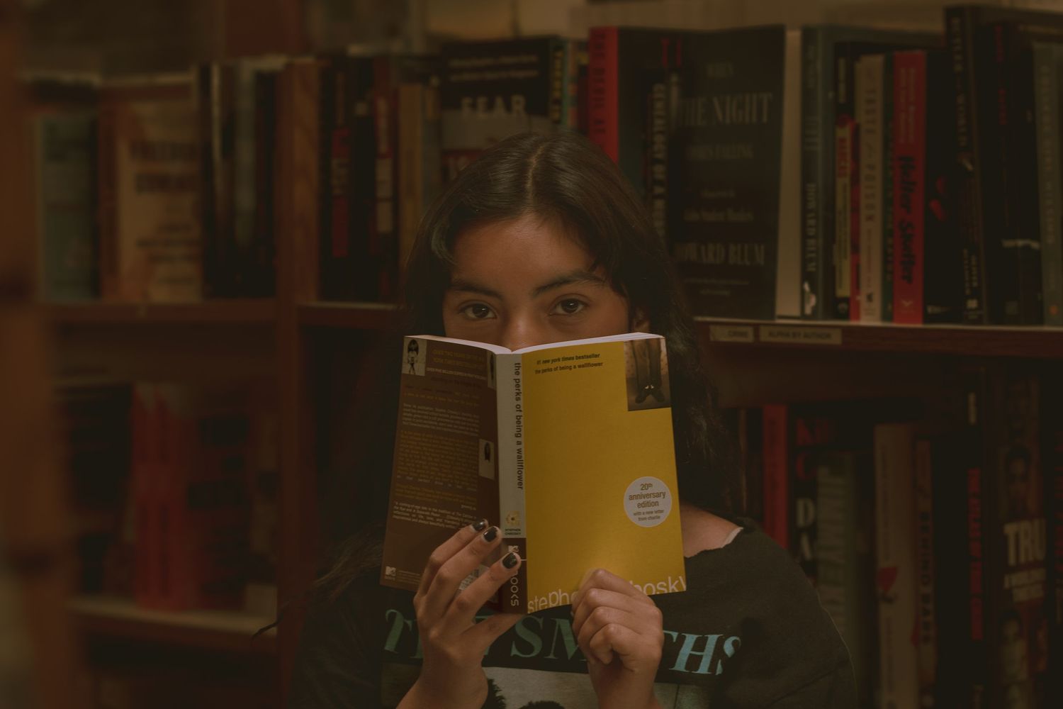 Senior girl posing with Perks of Being A Wallflower book in local Spokane Auntie's Bookstore for Class of 2025 Graduation session.