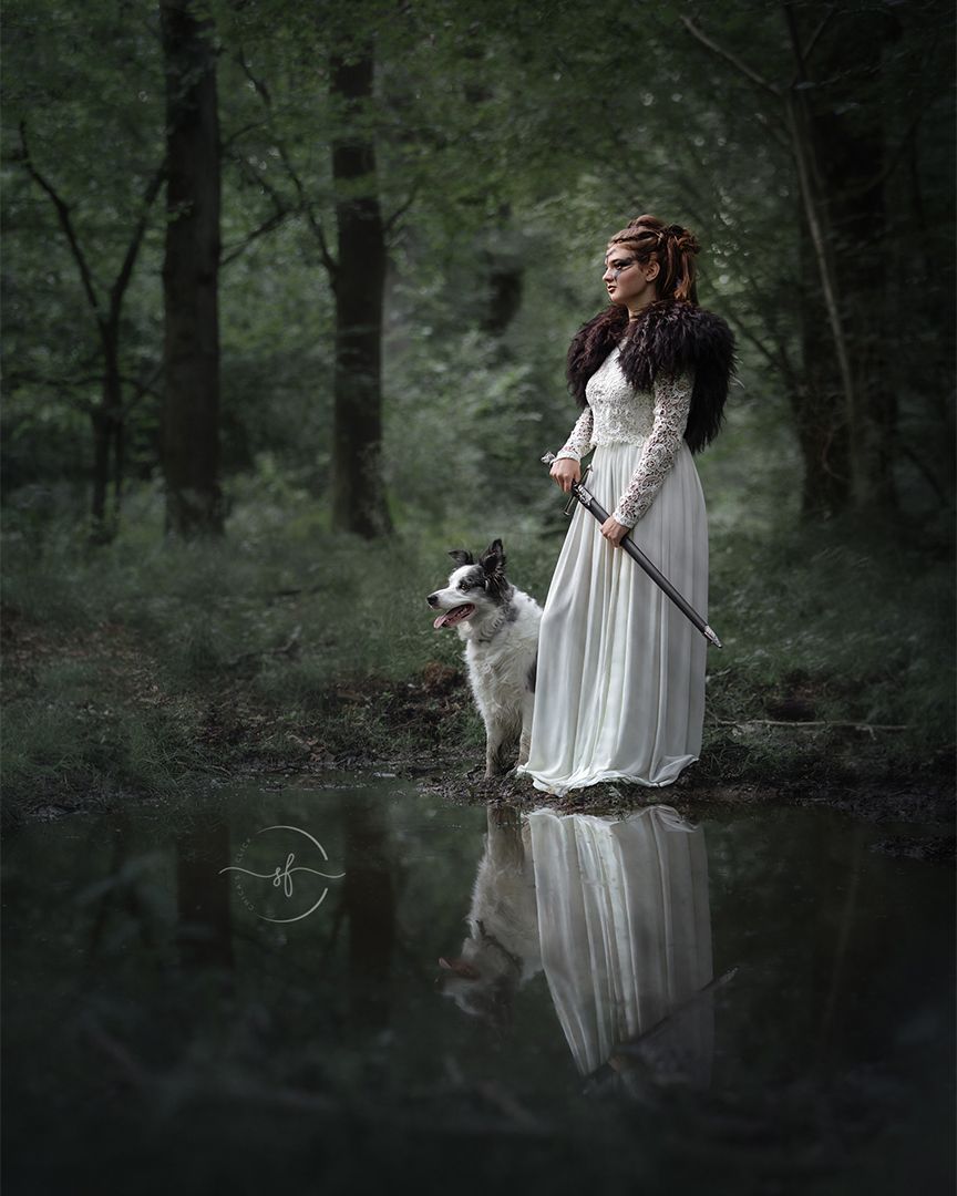 A woman in a flowing white dress sits serenely by a tranquil pond in a misty forest setting.
