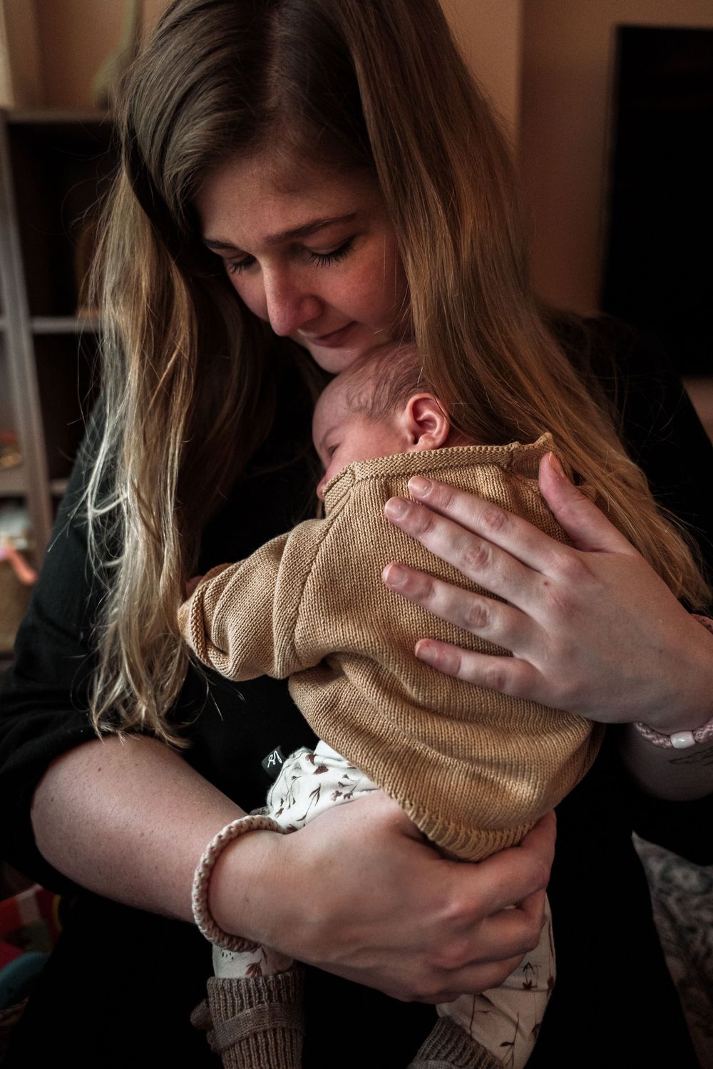 A tender moment as a woman in dark clothing holds and gazes lovingly at a baby wearing a brown sweater.