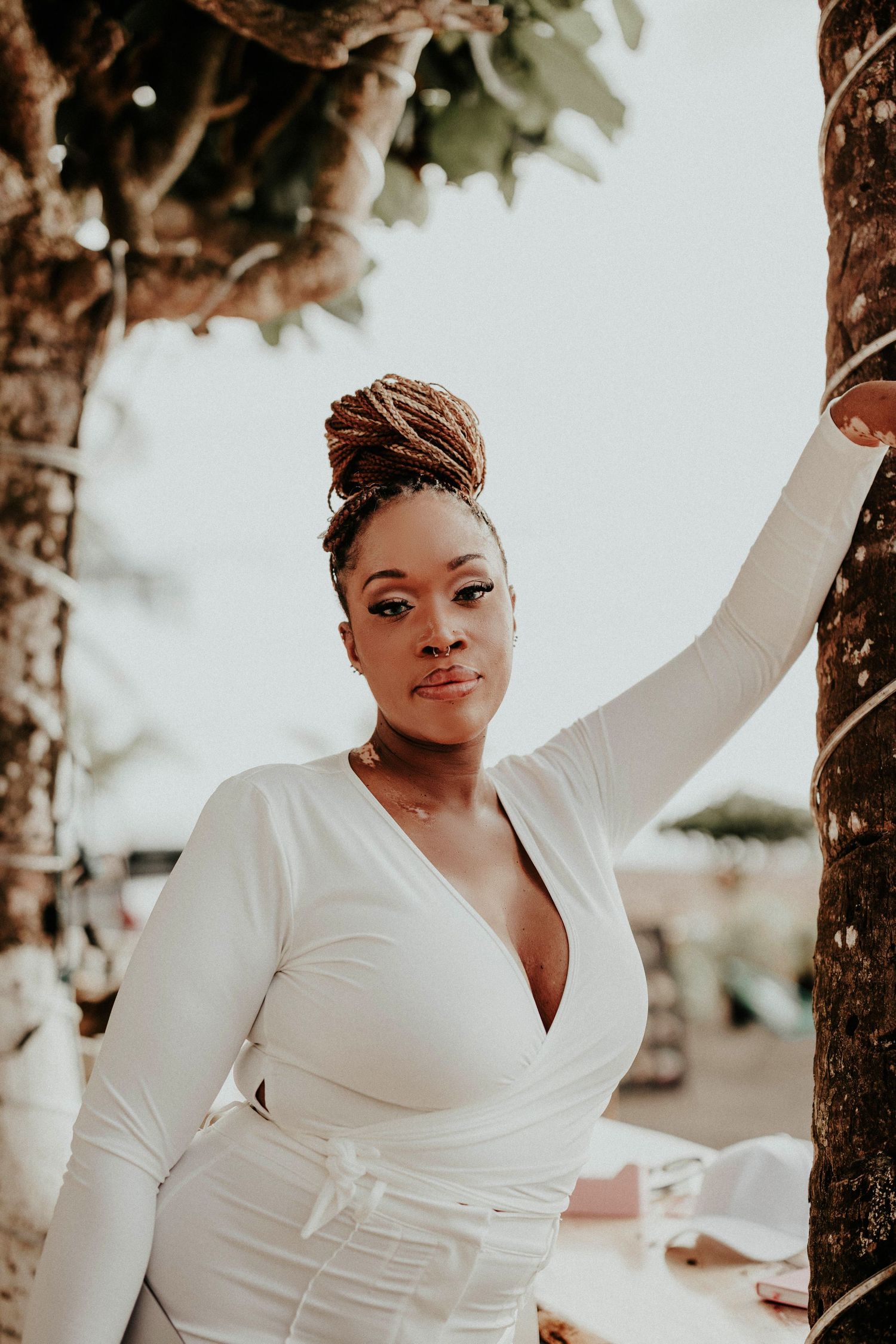 A person in a white wrap dress poses joyfully outdoors among trees on a sunny day.