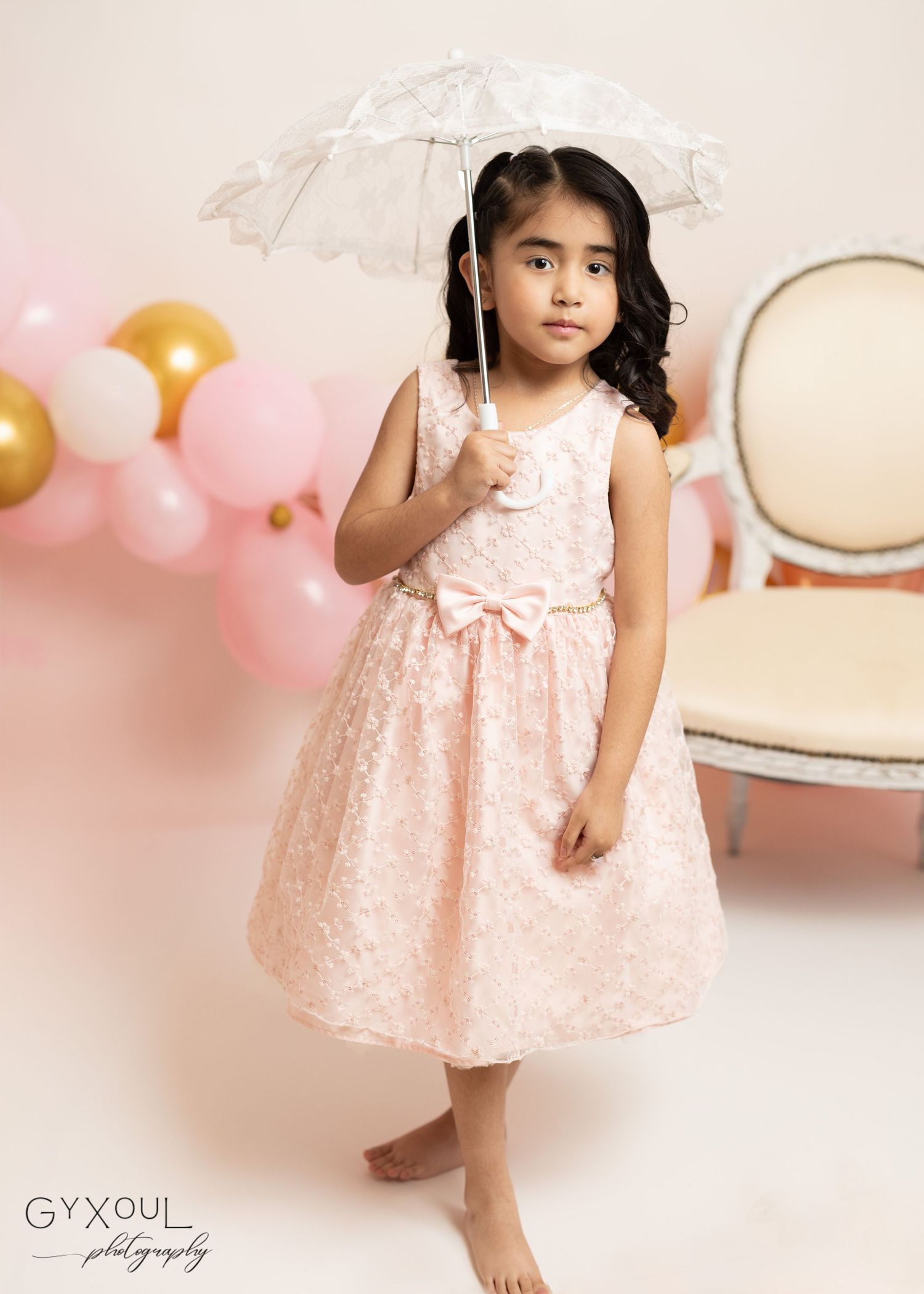 Family of four posing with pink and gold balloons in a professional photo studio setting.