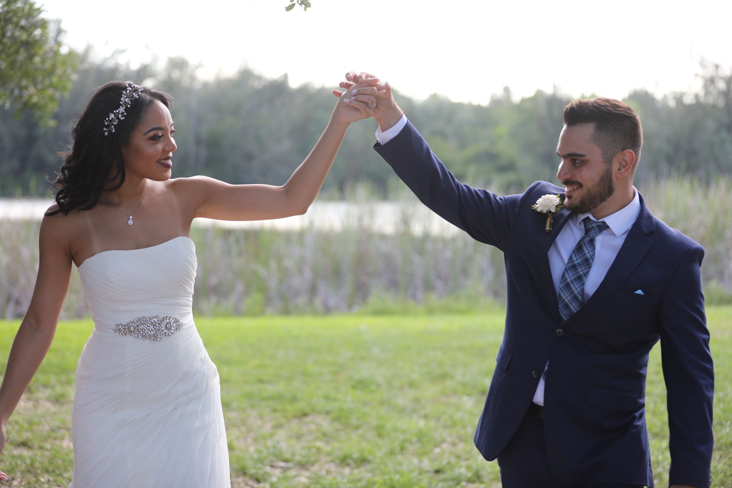 Newlyweds in formal attire dance joyfully in an outdoor setting.