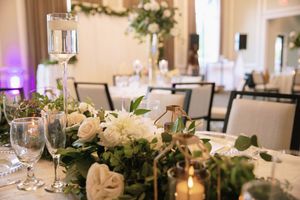 Elegant wedding reception table with white floral centerpiece, greenery garland, candles, and crystal glassware in a ballroom.