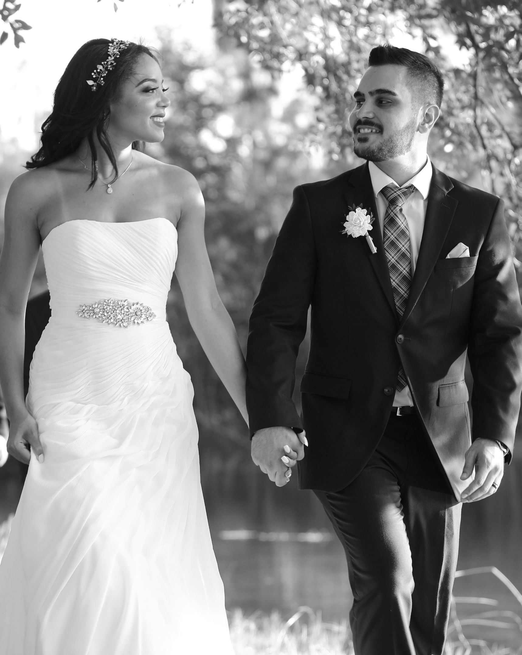 Black and white portrait of a bride and groom walking together in formal wedding attire.