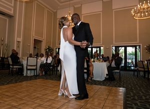 Couple shares first dance at elegant wedding reception in a grand ballroom with chandeliers and guests seated nearby.
