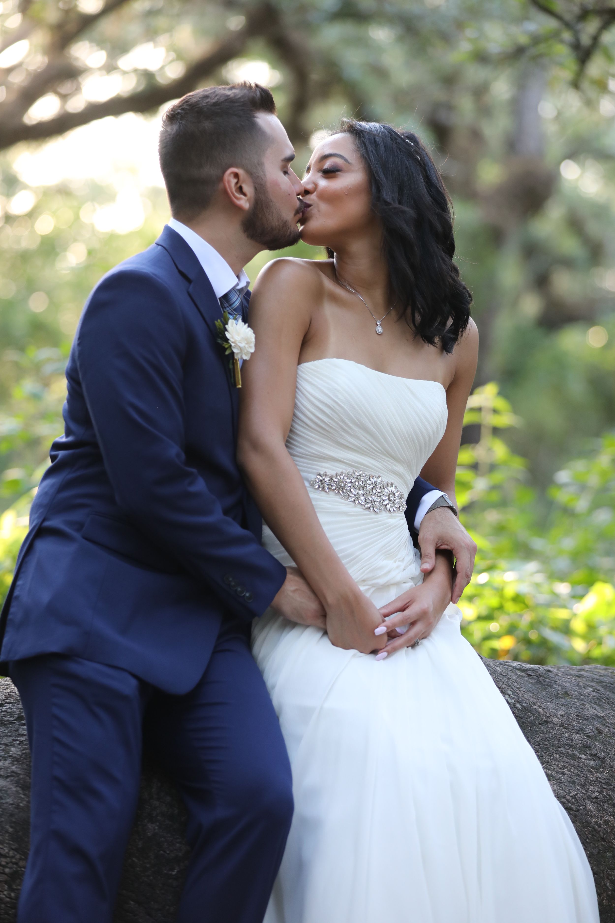 A romantic wedding moment between a bride in white and groom in navy sharing a kiss in a garden setting.
