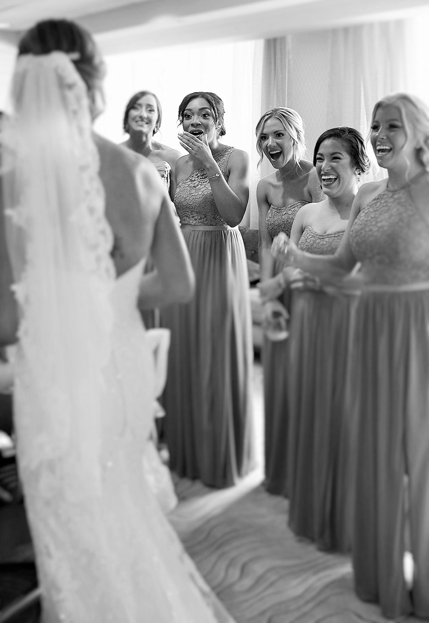 Bridesmaids in matching gray dresses react emotionally to seeing the bride for the first time.
