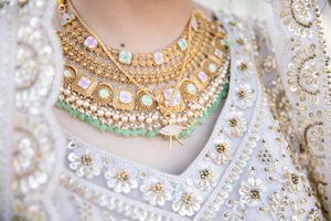 Close-up of ornate Indian bridal gold necklaces with pastel gems layered over an embroidered white lehenga.