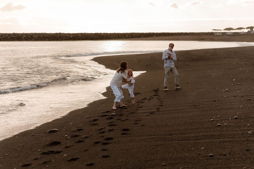Two people in white uniforms practice martial arts on a black sand beach at sunset.
