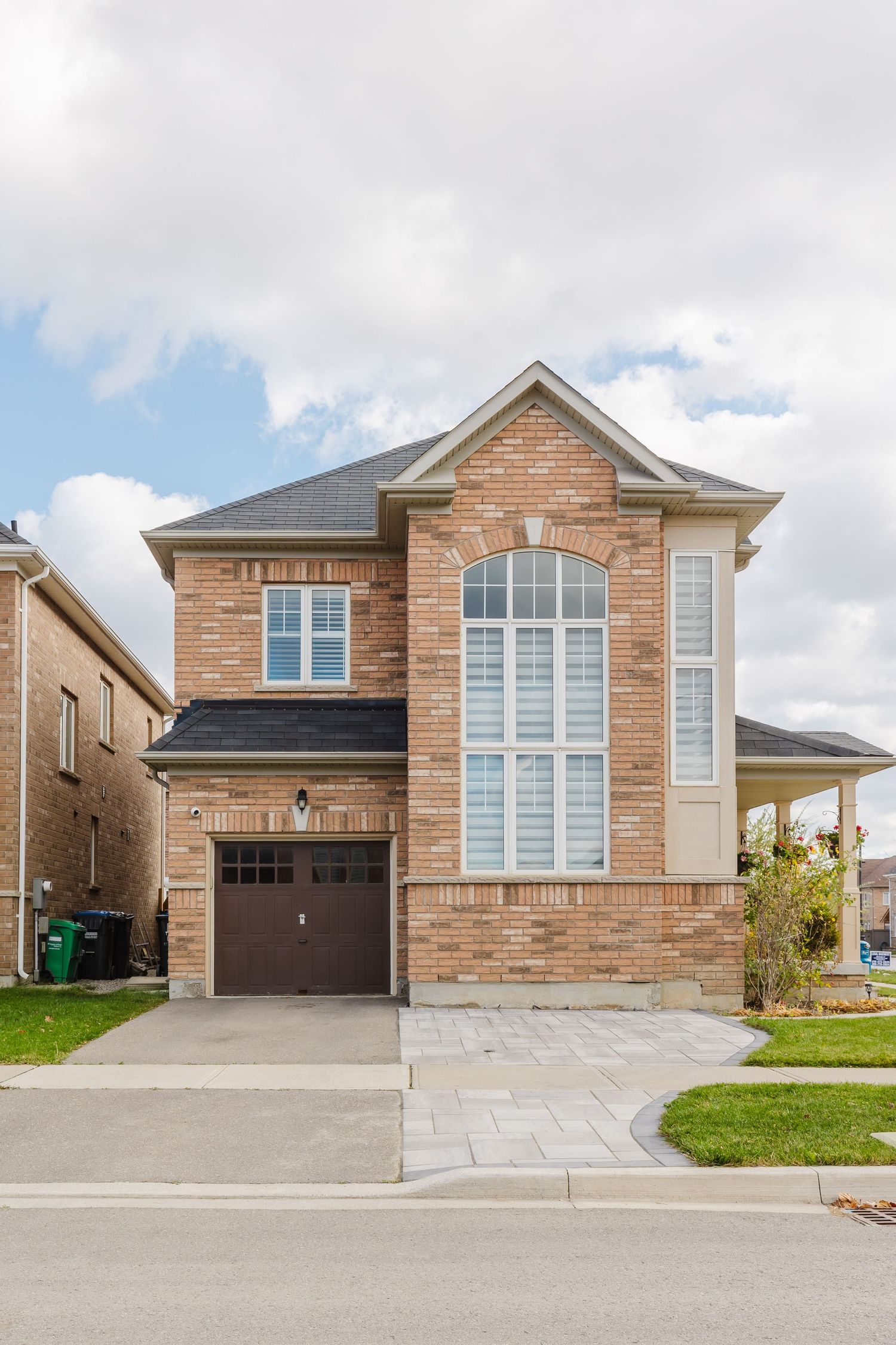 A two-story brick home with a single-car garage, arched window, and paved driveway in a suburban neighborhood.
