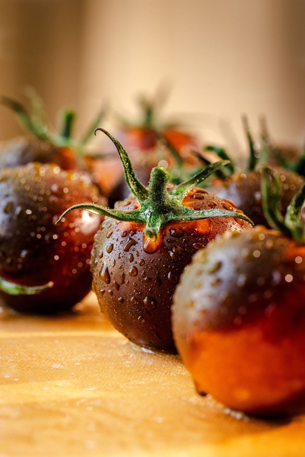 Close-up of fresh dark cherry tomatoes with water droplets on a wooden cutting board.